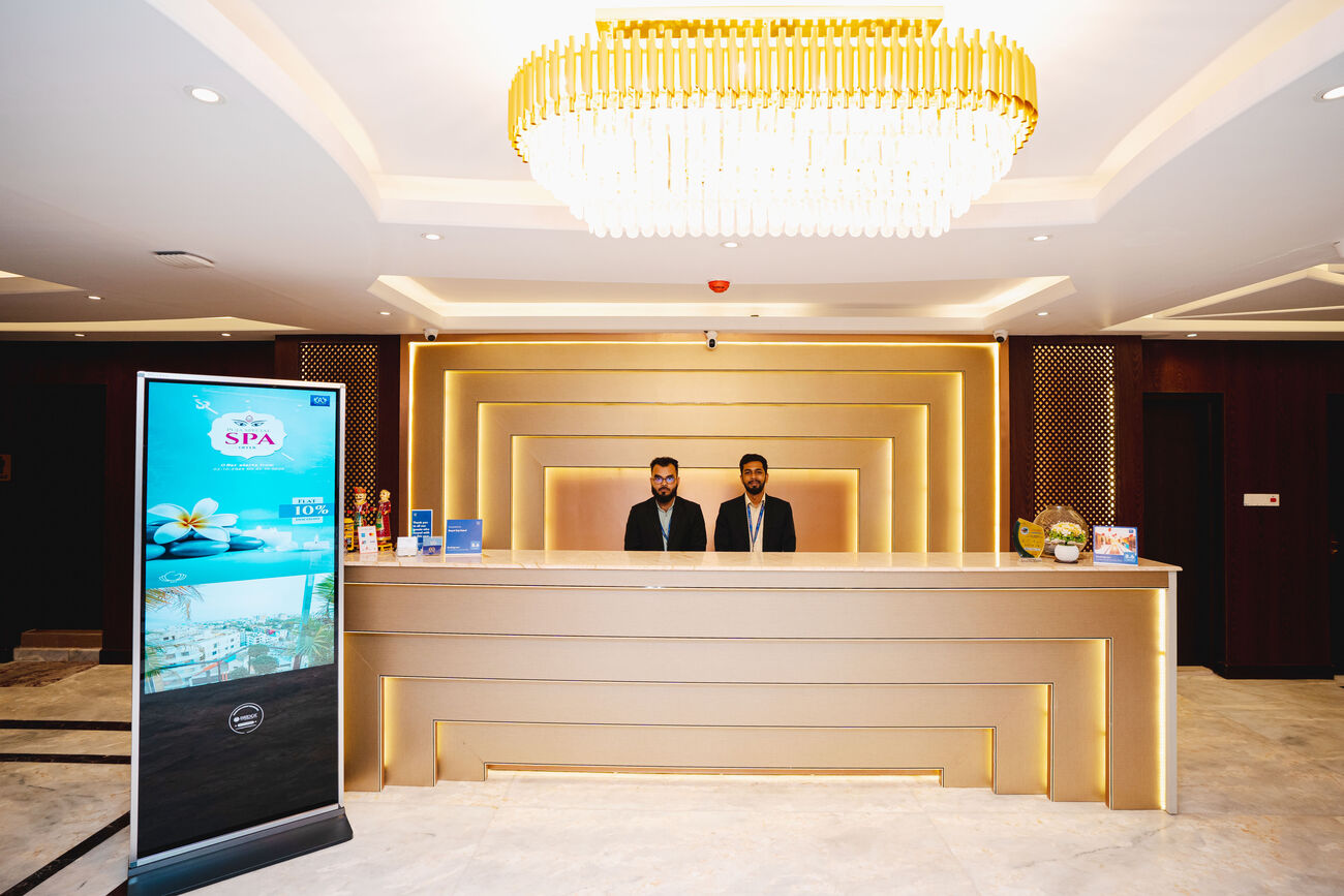 The front desk at night under a long gold chandelier, two staff on duty.