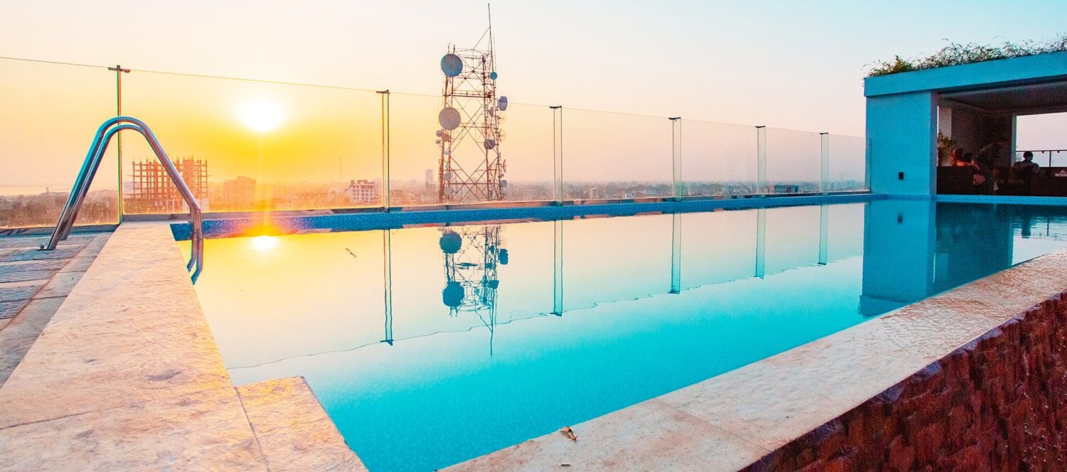 The rooftop infinity pool at Royal Raj at sunset, water running to the edge above the Rajshahi skyline.