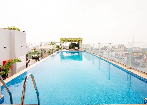 The rooftop pool in daylight, loungers along the deck above the city.