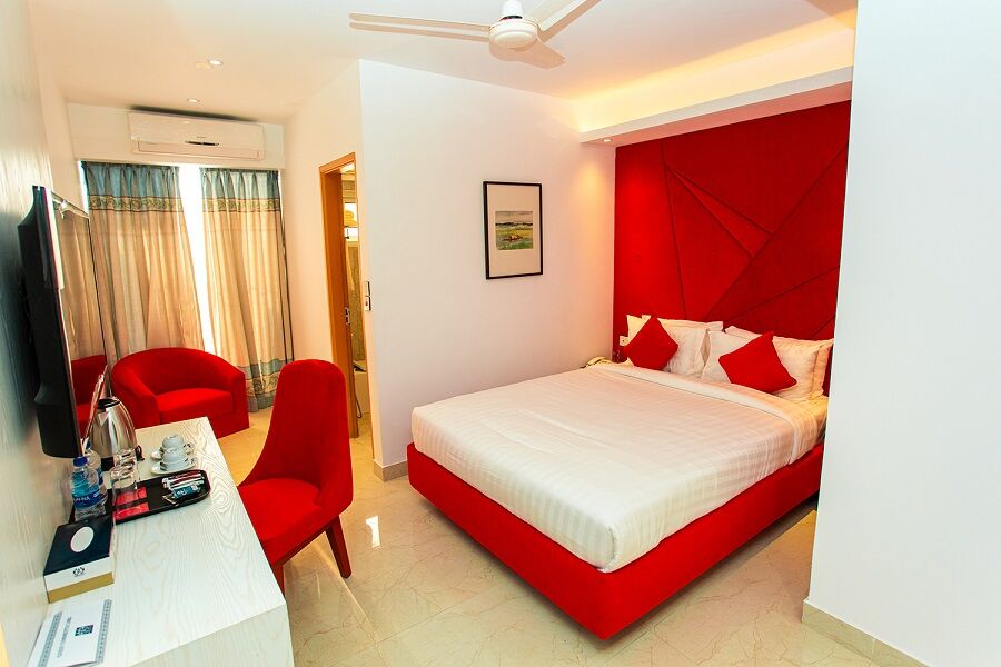 Deluxe Single room with a low bed against a red wall and a pair of armchairs.